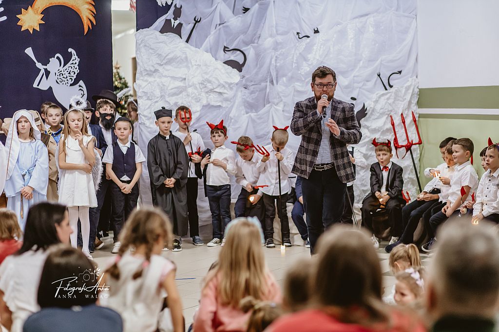 Przemawia dyrektor szkoły, w tle dzieci w strojach aniołów.