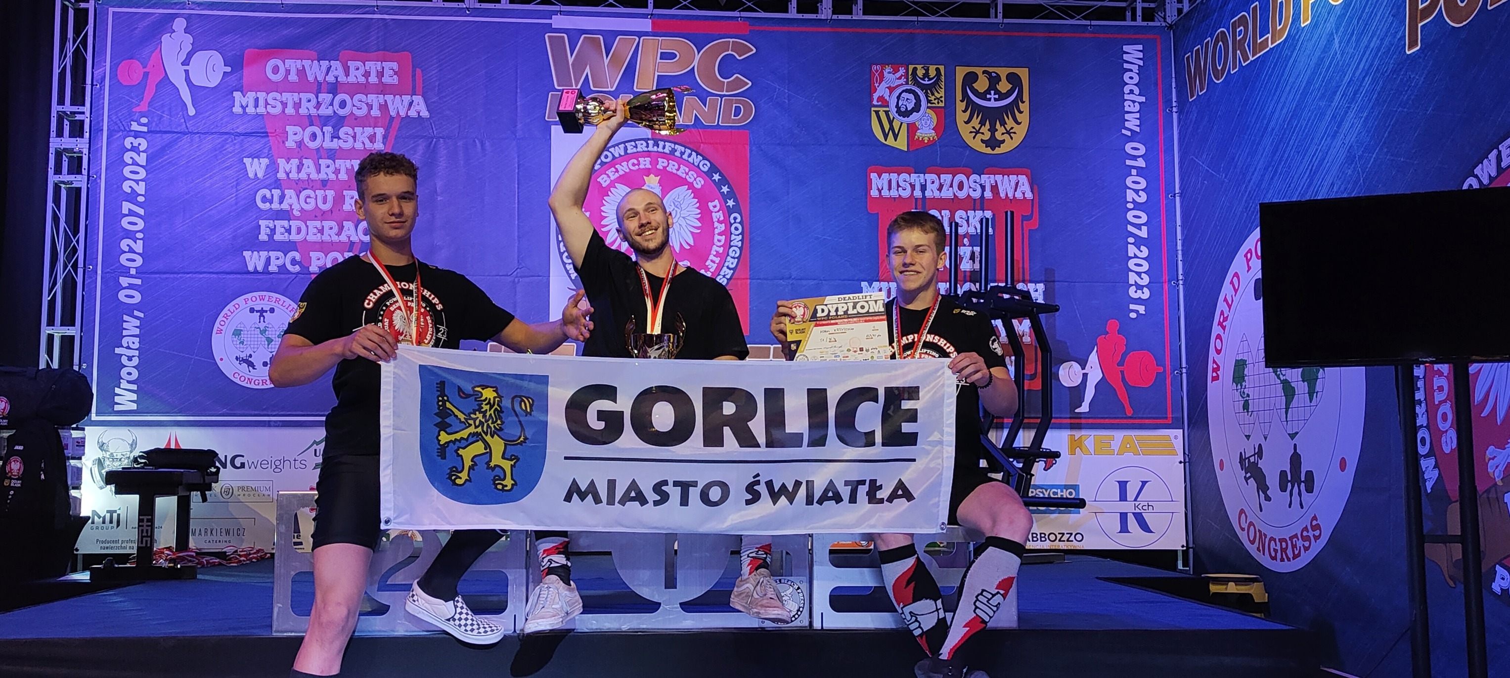 Huberyt Wójcikiewicz, Przemysław Stec i Adam Krzyszycha z flagą Gorlice Miasto Światła
