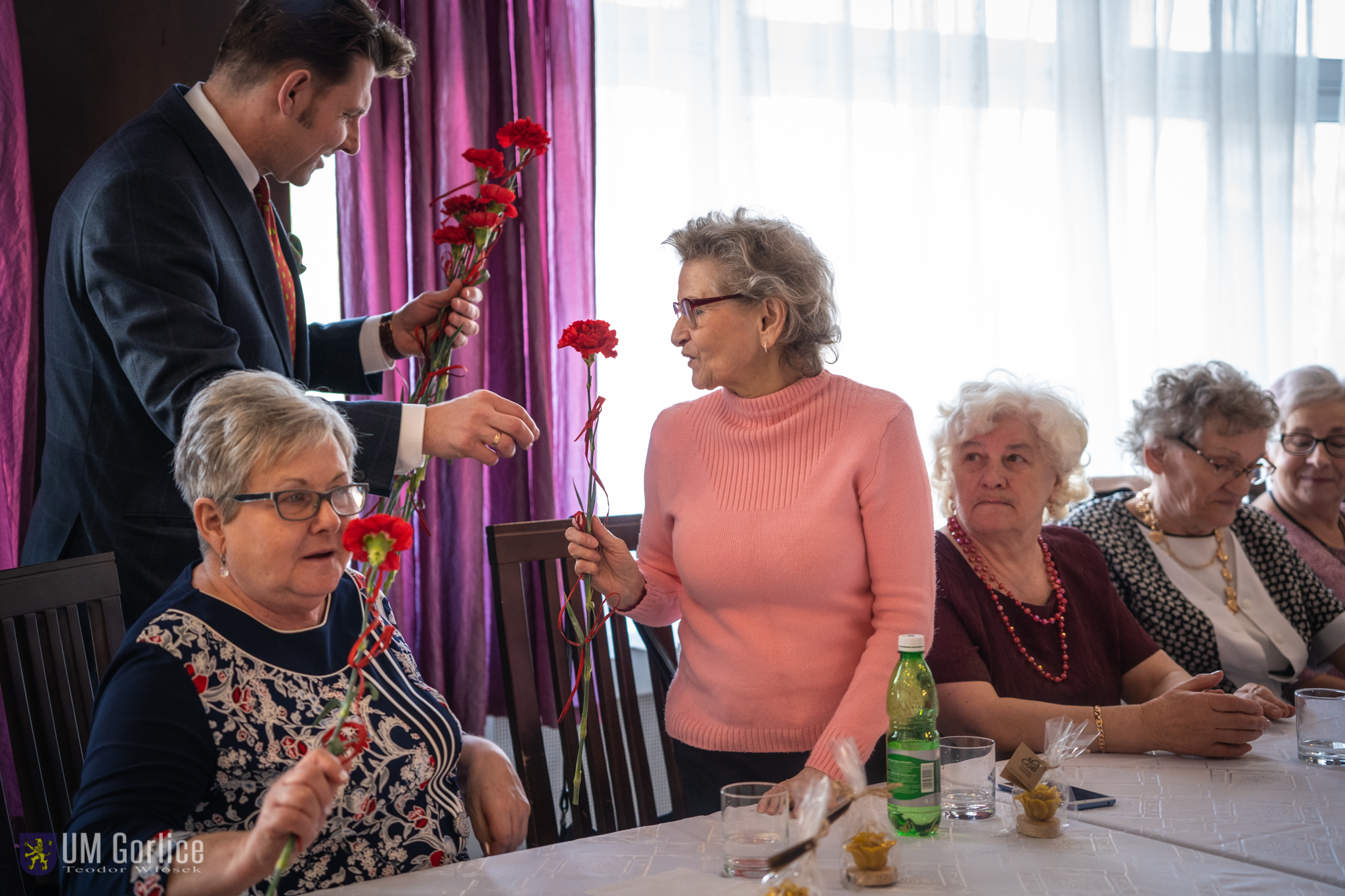 Burmistrz Rafał Kukla wręczający kwiaty z okazji Dnia Kobiet, podczas spotkania gorlickiego Stowarzyszenia Seniorów
