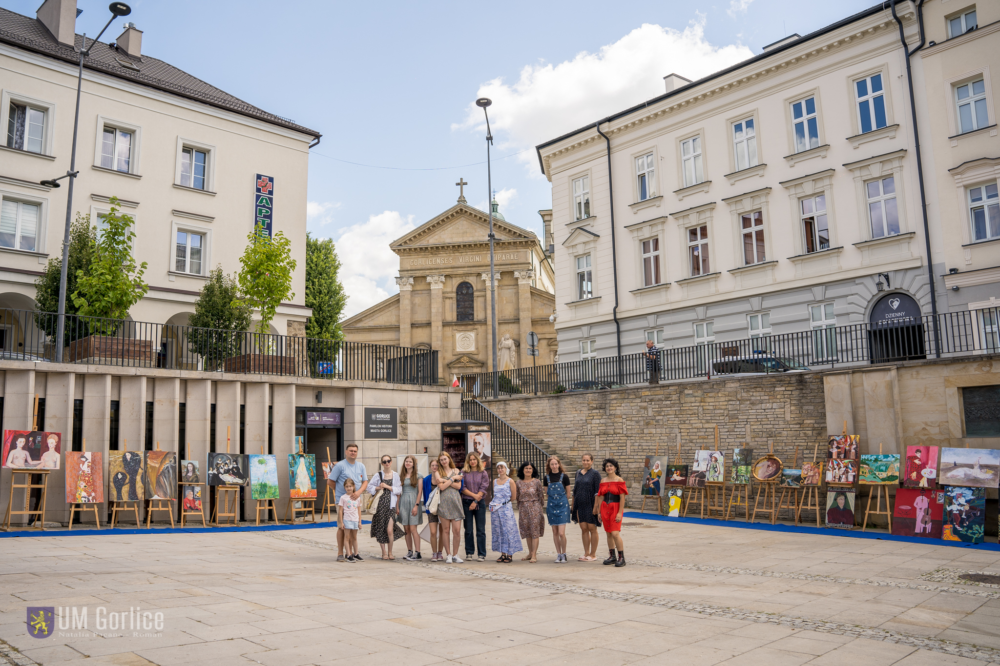 Atryści na tle obrazów na sztalugach na gorlickim Rynku - wystawa "Chodź na dzieło!"