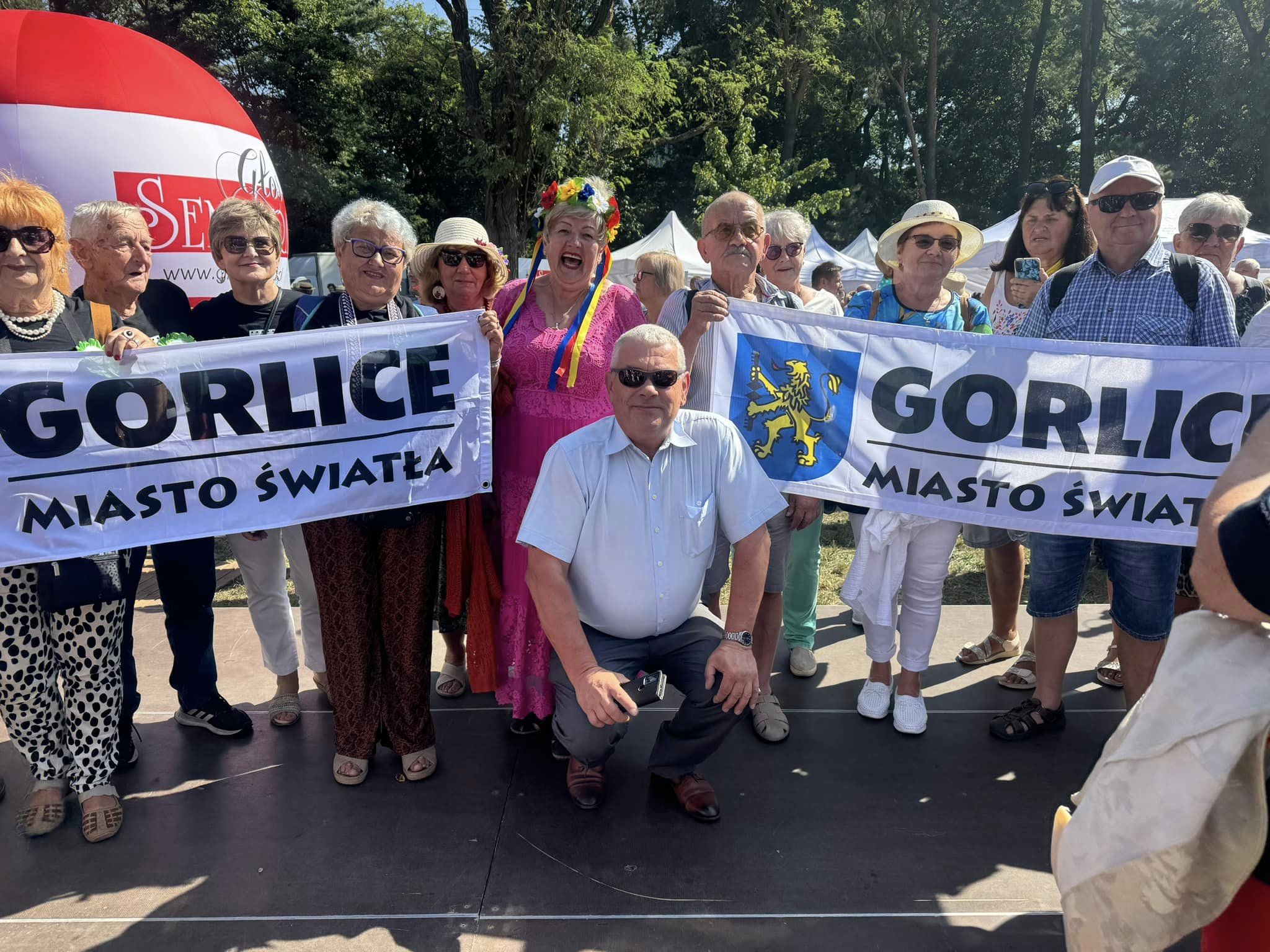 Seniorzy z flagą Miasta Światła w pochodzie w Krakowie.