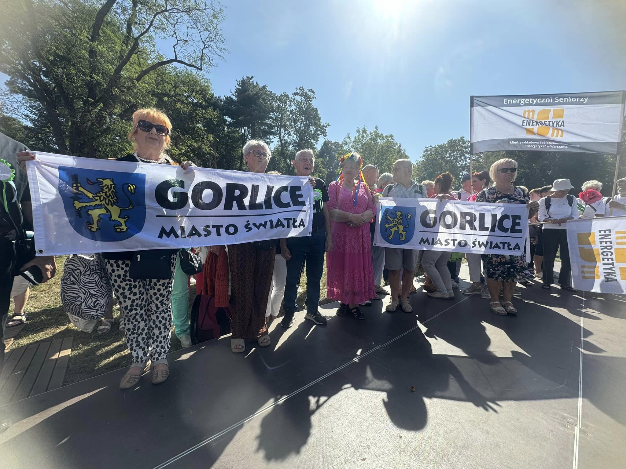 Seniorzy z flagą Miasta Światła w pochodzie w Krakowie.