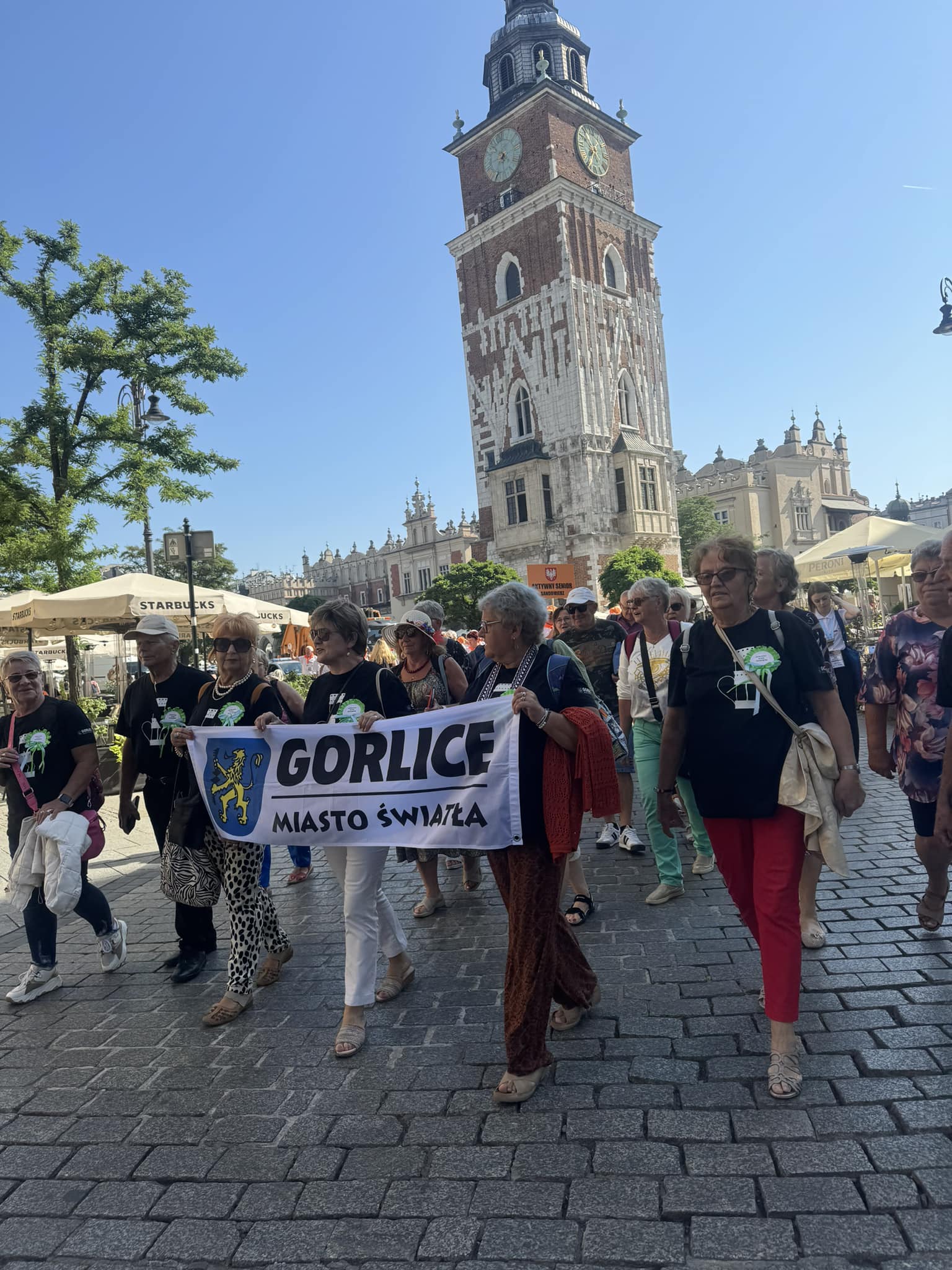 Seniorzy z flagą Miasta Światła w pochodzie w Krakowie.