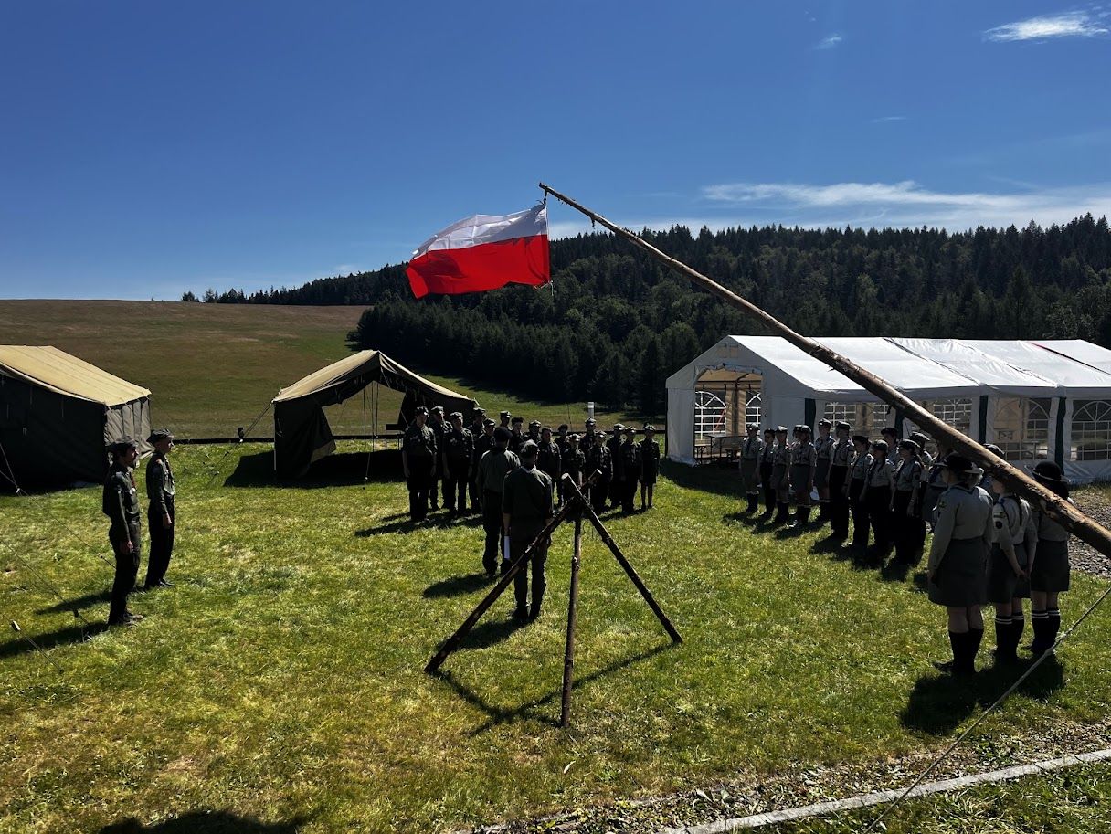 Obóz harcerski, w tle biało-czerowna flaga.