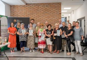 Zdjęcie grupowe uczetników wernisażu, w tle prace.
