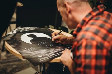 Gość składa autograf na plakacie wydarzenia.